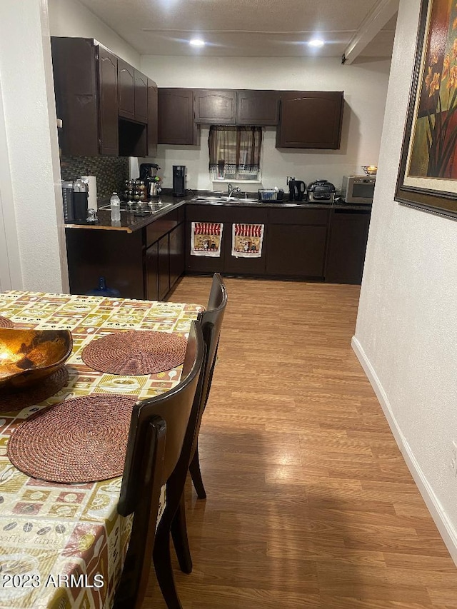 kitchen with dark brown cabinets, light wood-type flooring, and tasteful backsplash