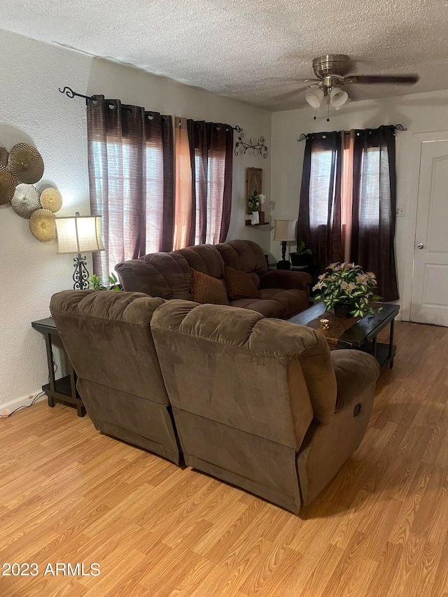 living room featuring light hardwood / wood-style flooring, ceiling fan, and a textured ceiling