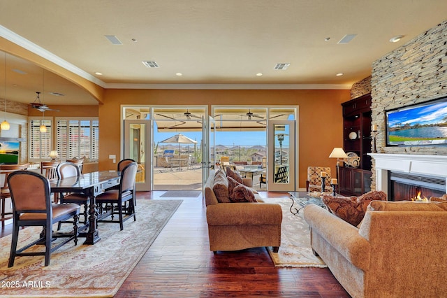 living area featuring a fireplace, visible vents, ornamental molding, a ceiling fan, and wood finished floors