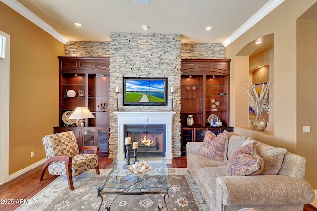 living area featuring baseboards, a glass covered fireplace, wood finished floors, and crown molding