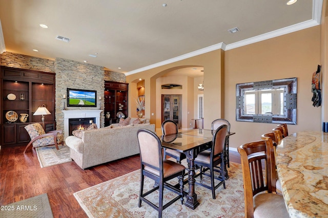 dining area with arched walkways, crown molding, visible vents, a large fireplace, and wood finished floors