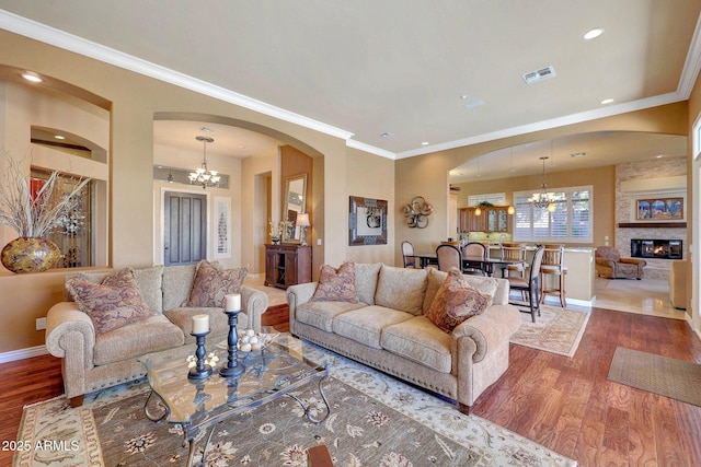 living area with a chandelier, a large fireplace, visible vents, and wood finished floors