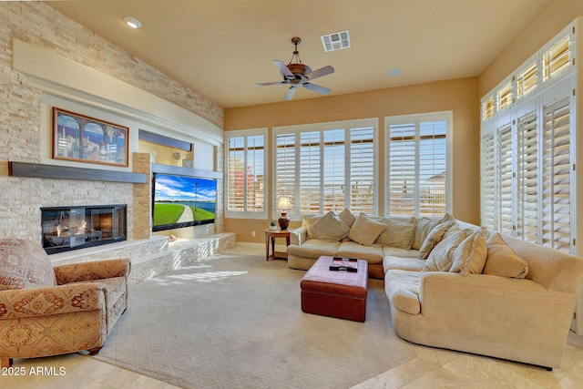 tiled living area featuring ceiling fan, visible vents, and a stone fireplace