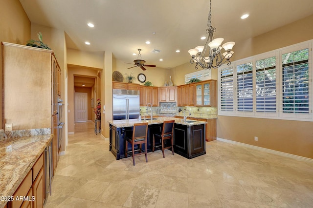 kitchen featuring a center island with sink, a breakfast bar area, backsplash, a sink, and stainless steel built in refrigerator