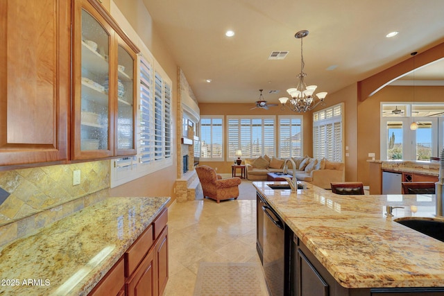 kitchen with backsplash, a sink, light stone countertops, dishwasher, and ceiling fan with notable chandelier