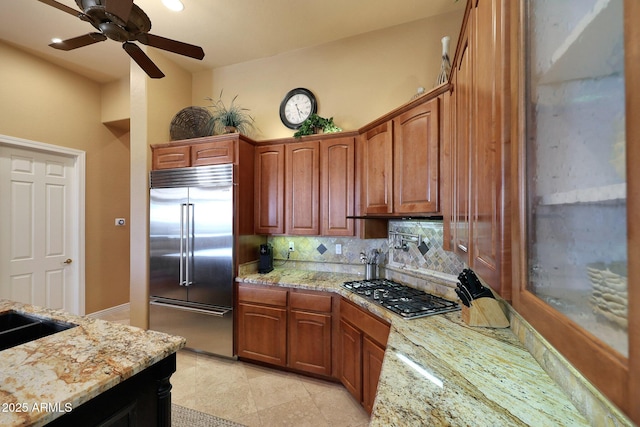 kitchen featuring ceiling fan, light stone counters, stainless steel appliances, brown cabinets, and tasteful backsplash