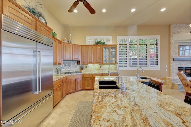 kitchen featuring a stone fireplace, light stone counters, stainless steel appliances, a sink, and backsplash