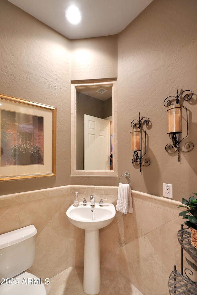 half bath featuring toilet, tile patterned flooring, and a textured wall