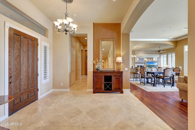 foyer entrance with arched walkways, baseboards, and an inviting chandelier