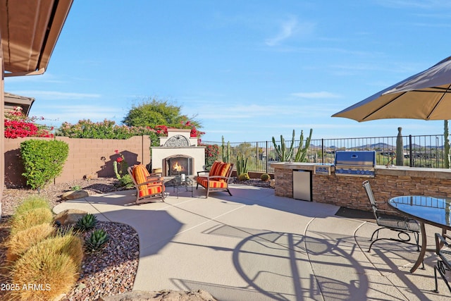 view of patio / terrace featuring a grill, fence, a lit fireplace, and area for grilling