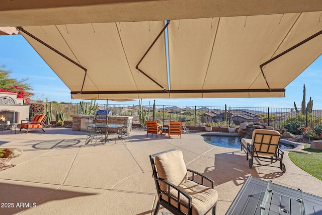 view of patio with a warm lit fireplace, fence, a fenced in pool, and area for grilling