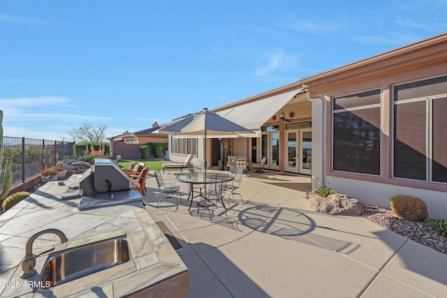 view of patio with french doors, a sink, outdoor dining area, and fence