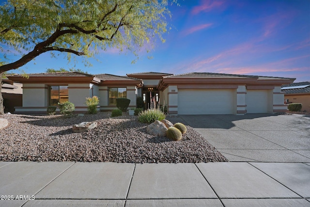 prairie-style home featuring concrete driveway, an attached garage, and stucco siding