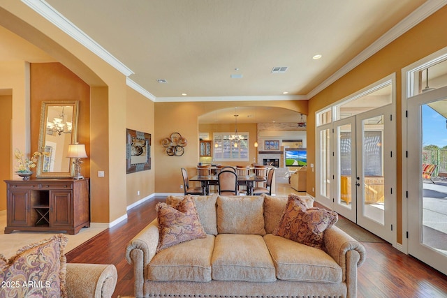 living room featuring crown molding, wood-type flooring, visible vents, an inviting chandelier, and baseboards