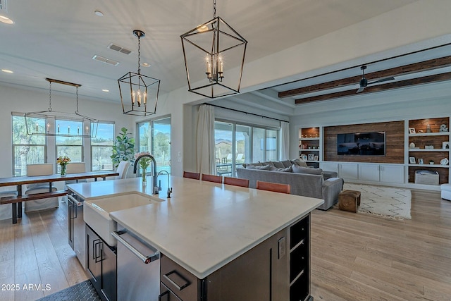 kitchen with light wood-type flooring, sink, pendant lighting, a center island with sink, and built in features