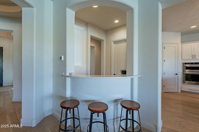 kitchen featuring white cabinets, a kitchen breakfast bar, stainless steel double oven, and light hardwood / wood-style floors