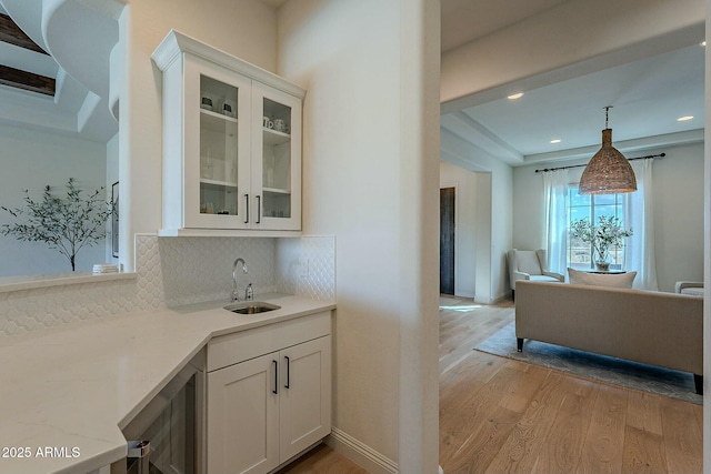 kitchen with sink, hanging light fixtures, tasteful backsplash, light hardwood / wood-style floors, and white cabinetry