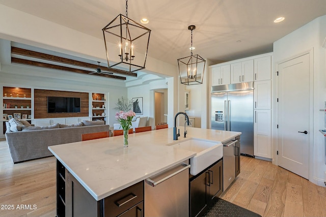 kitchen featuring built in shelves, stainless steel appliances, sink, decorative light fixtures, and a center island with sink