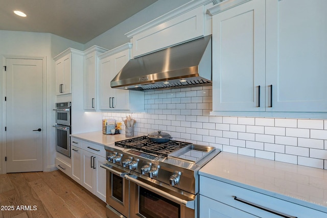 kitchen with white cabinetry, stainless steel appliances, wall chimney range hood, and light wood-type flooring