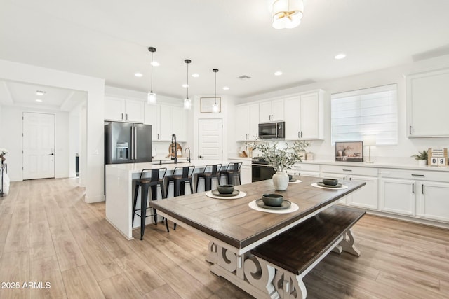 kitchen with pendant lighting, appliances with stainless steel finishes, a kitchen island with sink, white cabinets, and light wood-type flooring