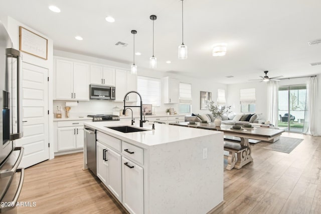 kitchen with sink, appliances with stainless steel finishes, white cabinetry, a kitchen island with sink, and decorative light fixtures