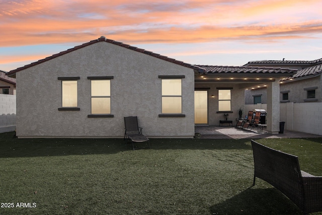 back house at dusk with a yard and a patio area