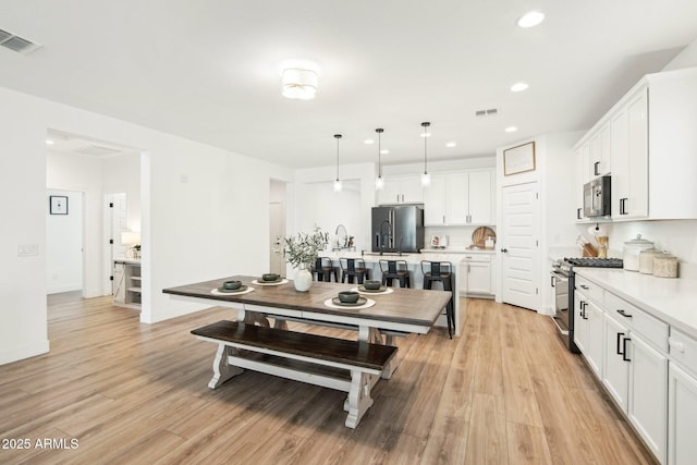 kitchen with pendant lighting, white cabinetry, stainless steel range with gas stovetop, light hardwood / wood-style floors, and black refrigerator with ice dispenser