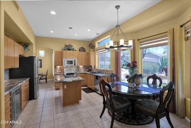 kitchen with a kitchen island, appliances with stainless steel finishes, decorative light fixtures, light tile patterned floors, and beverage cooler