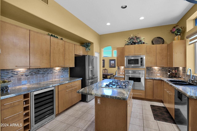 kitchen featuring stainless steel appliances, light stone counters, a center island, beverage cooler, and sink