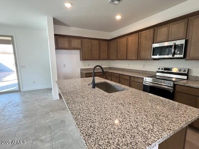 kitchen with light stone counters, sink, stainless steel appliances, and an island with sink