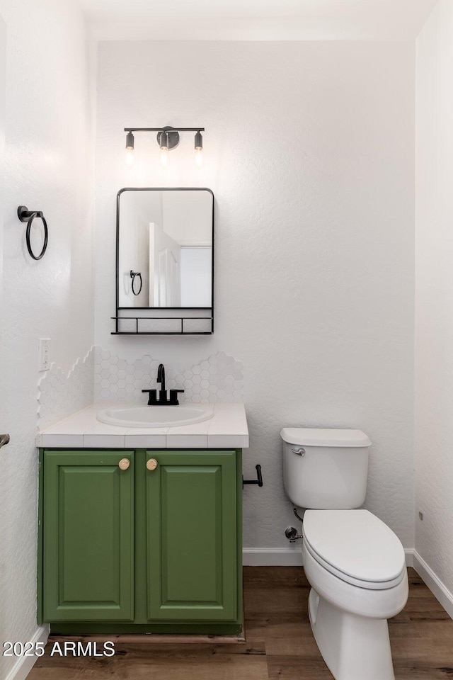 half bathroom featuring vanity, toilet, wood finished floors, decorative backsplash, and baseboards