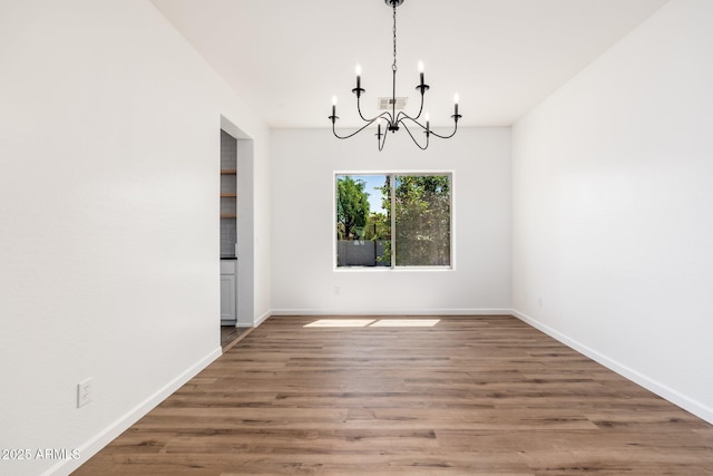 unfurnished dining area with visible vents, baseboards, a chandelier, and wood finished floors