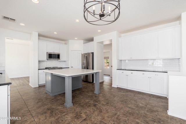 kitchen featuring visible vents, white cabinets, a chandelier, stainless steel appliances, and backsplash
