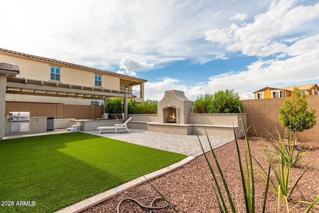 view of yard featuring a warm lit fireplace, a fenced backyard, a patio, and an outdoor kitchen