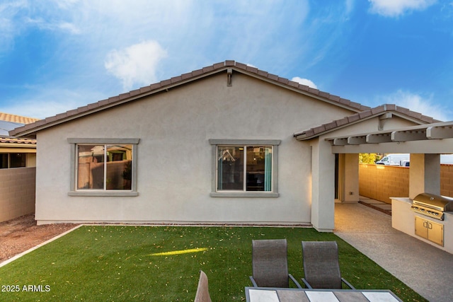 back of house featuring exterior kitchen, fence, a lawn, and stucco siding