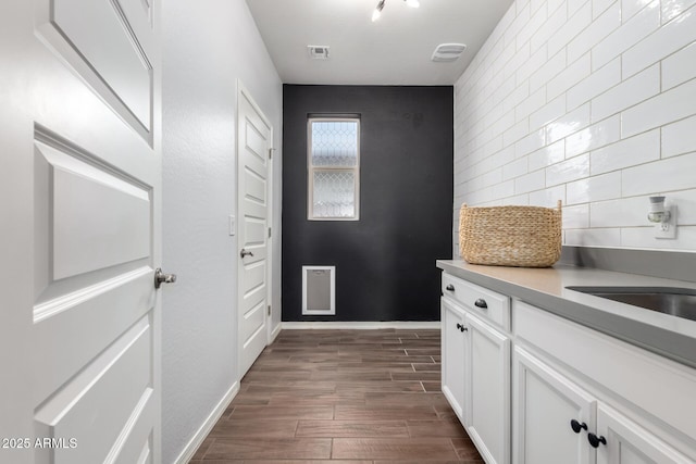 interior space featuring visible vents, white cabinets, decorative backsplash, wood tiled floor, and a sink