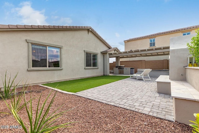 rear view of property featuring exterior kitchen, a pergola, a patio area, and stucco siding