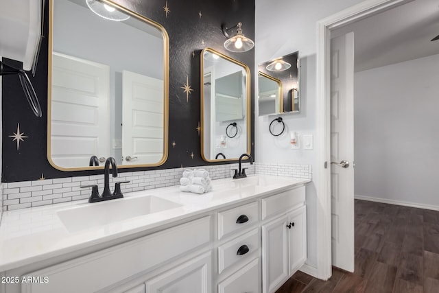 bathroom featuring wood finished floors, a sink, baseboards, backsplash, and double vanity