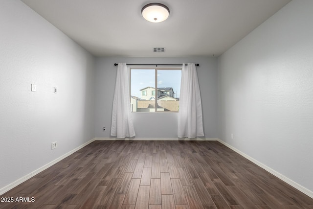 empty room featuring dark wood-style floors, visible vents, and baseboards