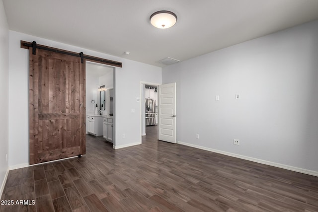 unfurnished bedroom featuring a barn door, connected bathroom, baseboards, and dark wood-style flooring