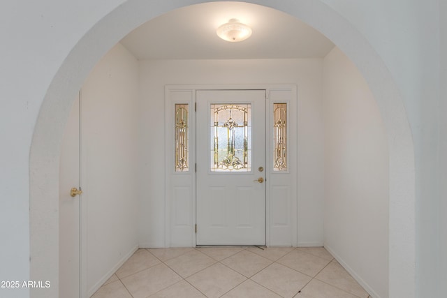 entrance foyer featuring light tile patterned floors, arched walkways, and baseboards