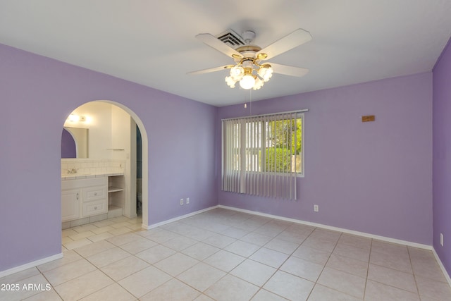 unfurnished bedroom with light tile patterned floors, baseboards, arched walkways, ceiling fan, and a sink