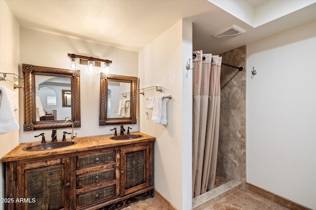 bathroom with a sink, baseboards, visible vents, and tiled shower