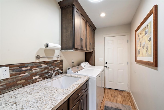 clothes washing area featuring a sink, baseboards, washer and dryer, cabinet space, and light wood finished floors