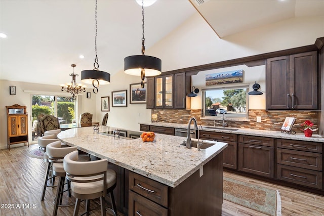 kitchen with pendant lighting, lofted ceiling, glass insert cabinets, a kitchen island with sink, and a sink