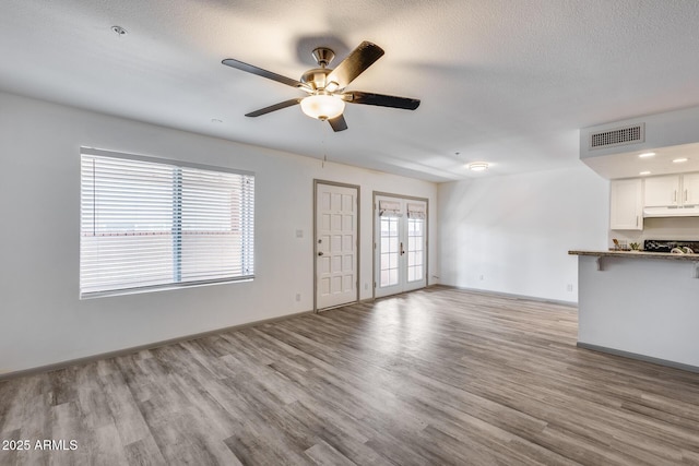 unfurnished living room featuring a textured ceiling, french doors, light wood-type flooring, and visible vents