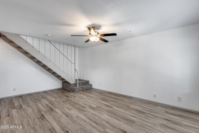 unfurnished living room featuring baseboards, light wood-style flooring, ceiling fan, stairs, and a textured ceiling