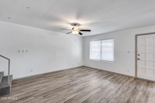 unfurnished living room featuring light wood-style flooring, stairs, ceiling fan, and a textured ceiling