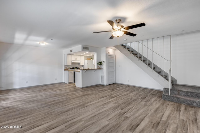 unfurnished living room with light wood finished floors, visible vents, and stairway