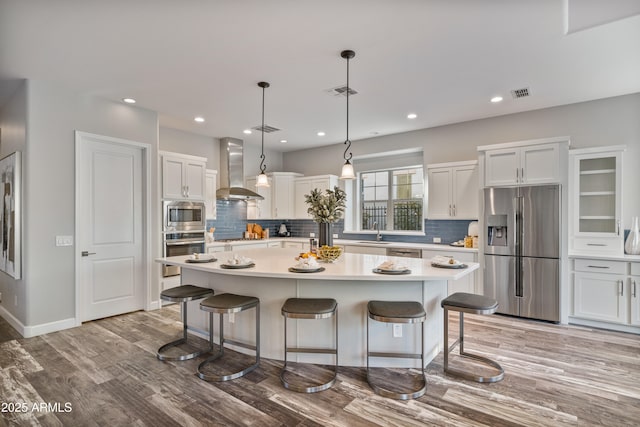 kitchen with white cabinets, sink, wall chimney exhaust hood, appliances with stainless steel finishes, and a kitchen island